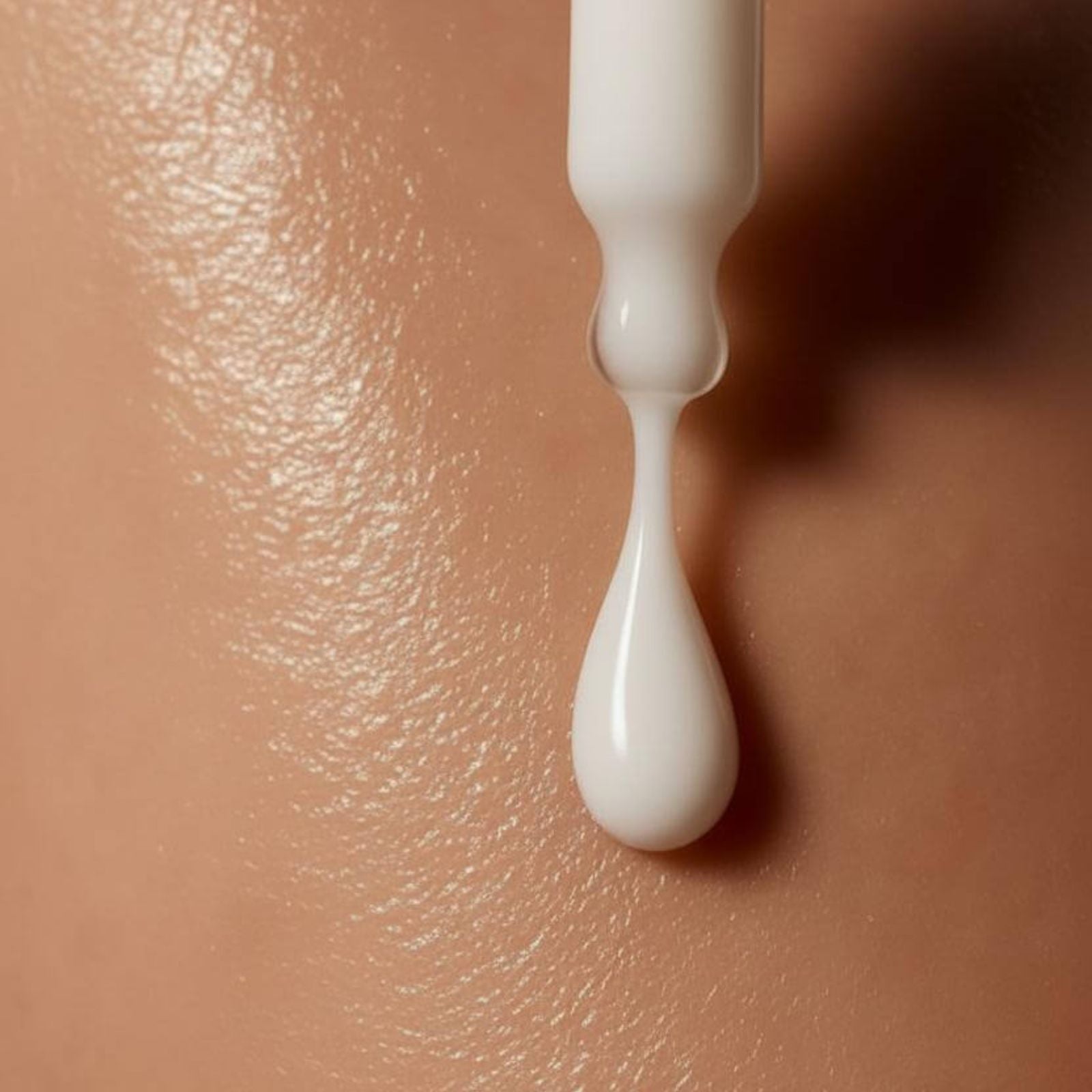 Close-up of Rewritten Beauty serum dropper releasing a droplet onto tan skin, highlighting product texture and hydration effect