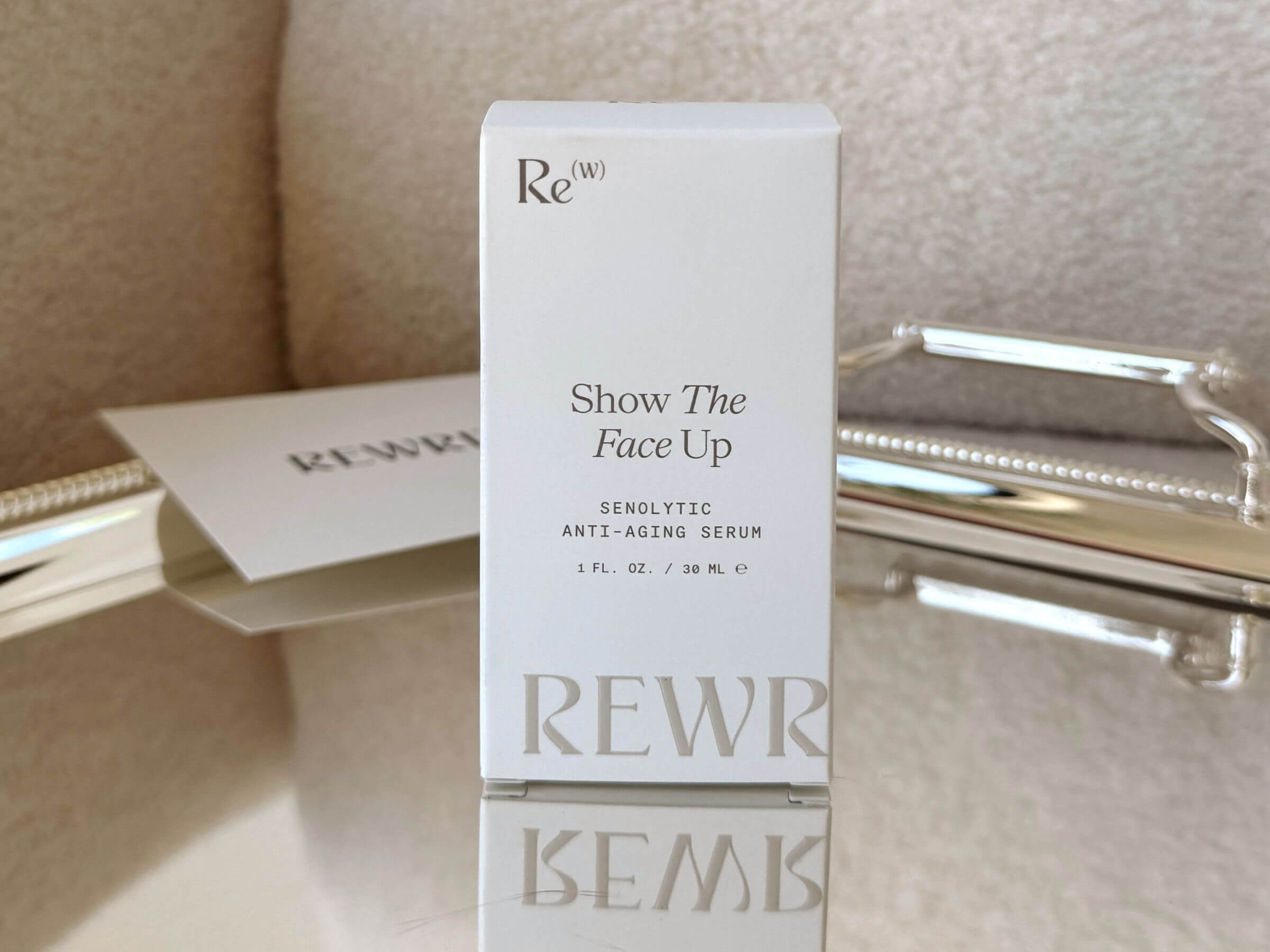 Rewritten Show The Face Up senolytic anti-aging serum packaging box displayed upright on a reflective surface with soft home background decor