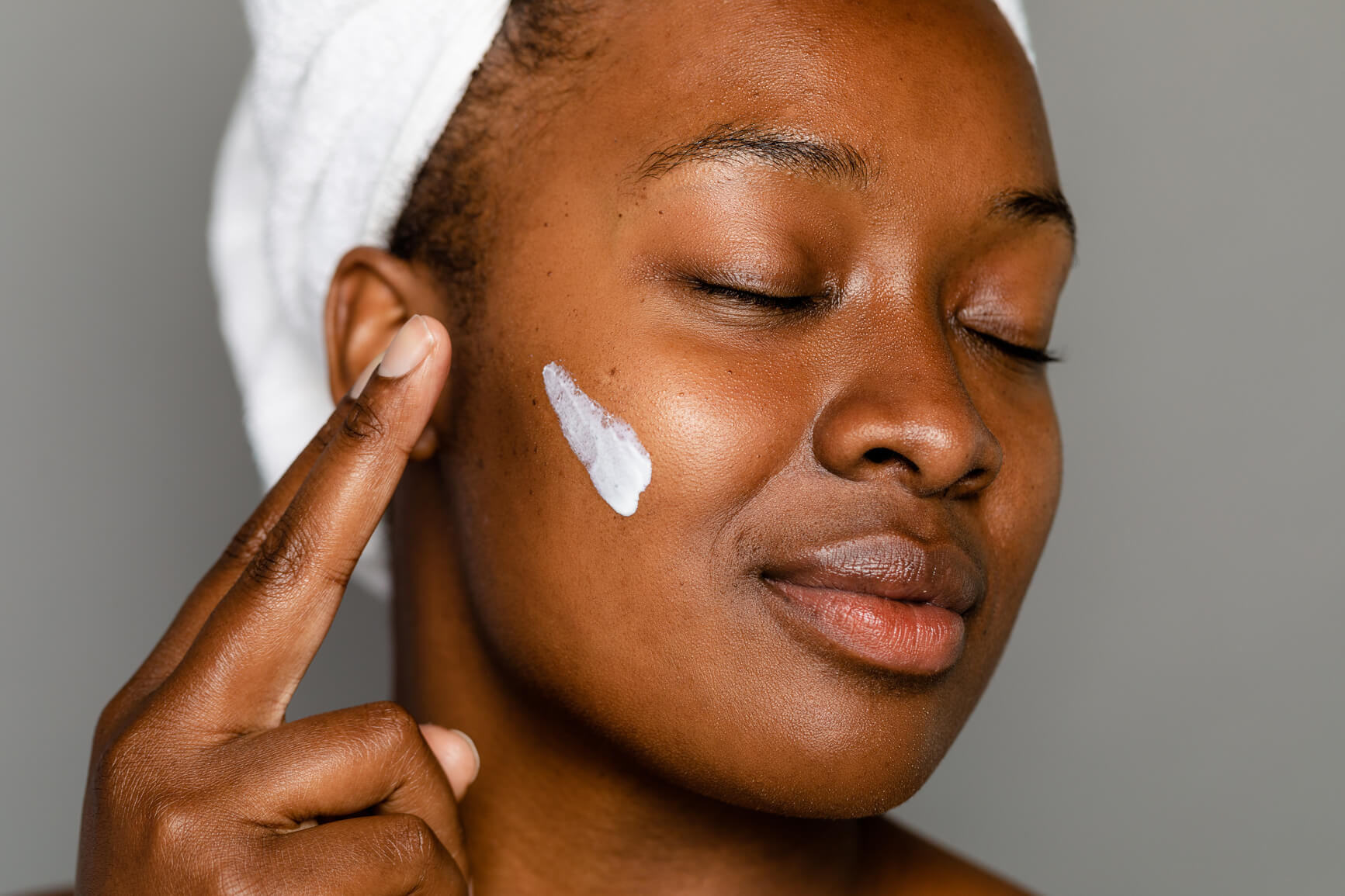 Woman with towel on head applying Rewritten Beauty skincare serum to her face with eyes closed.