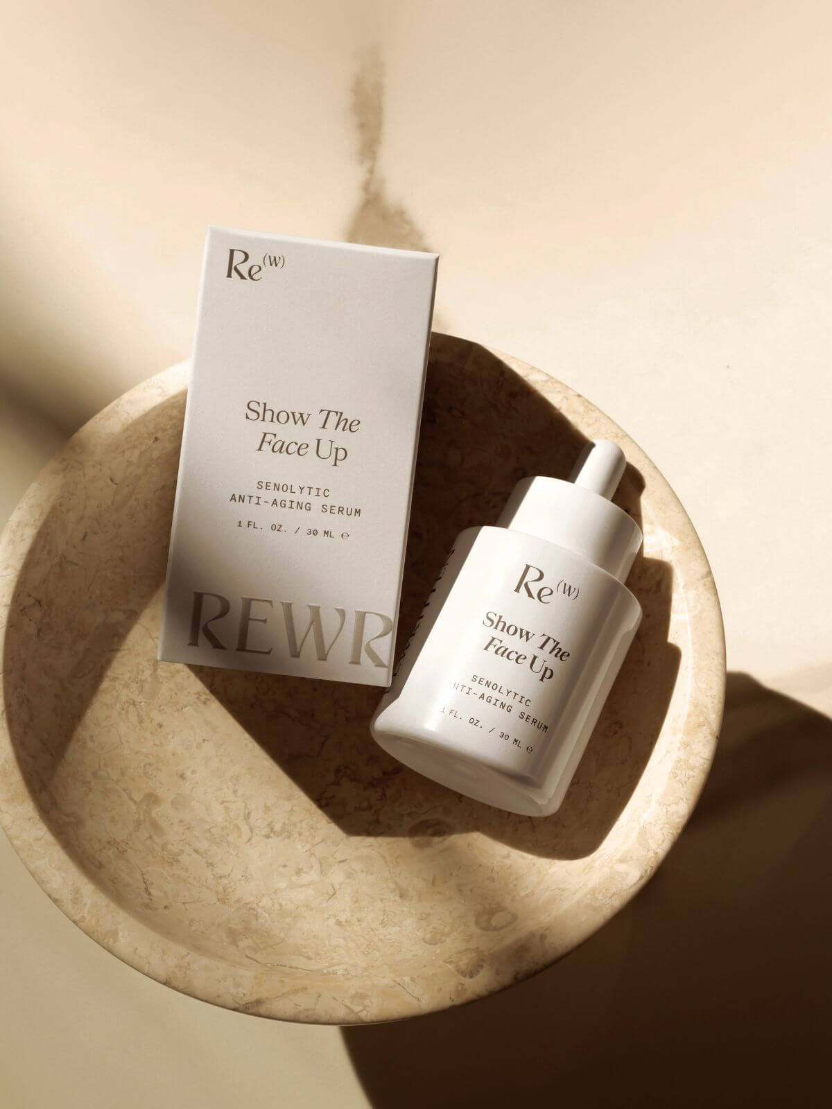 Rewritten Show The Face Up senolytic anti-aging serum and packaging box displayed on a stone dish with natural light and shadows